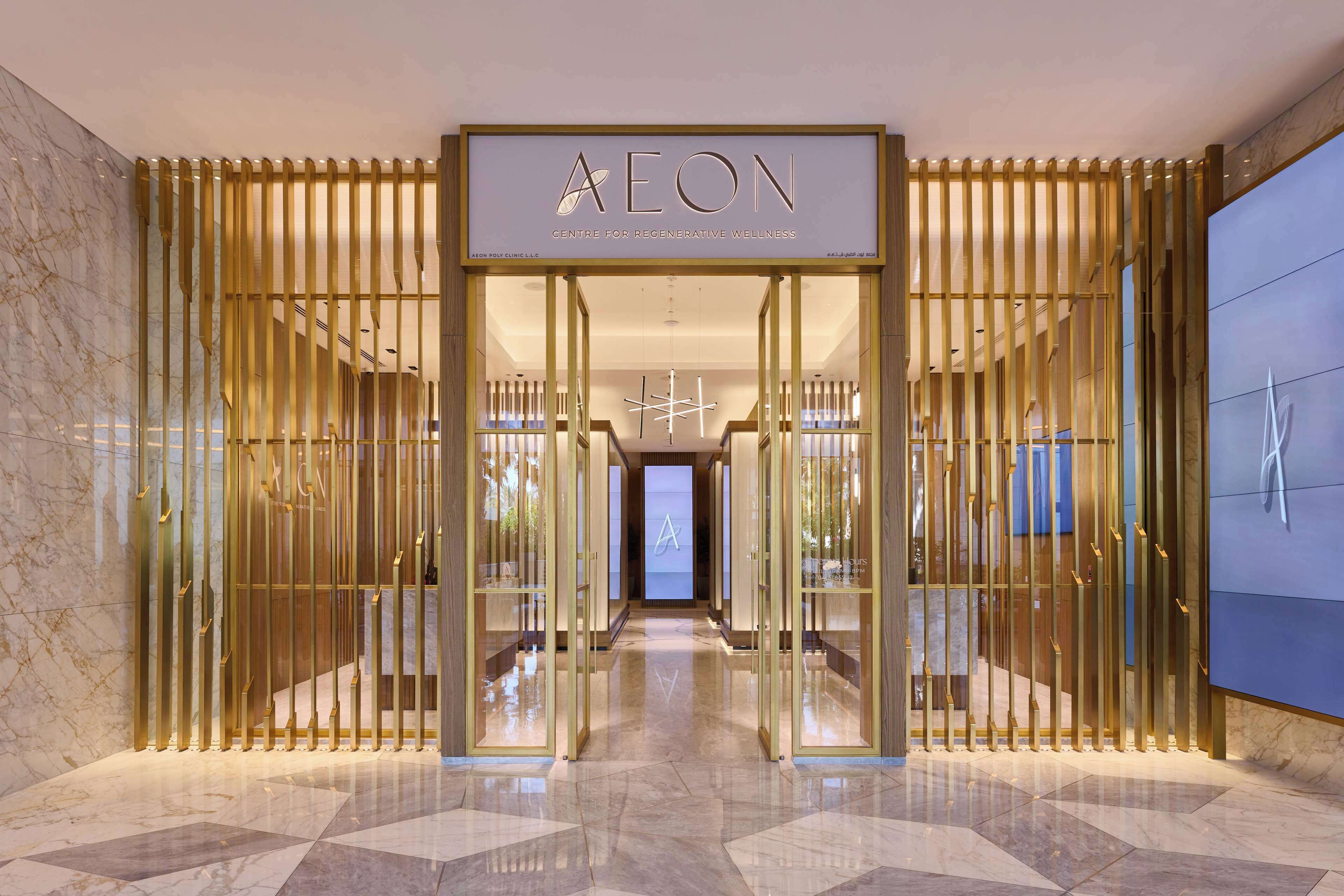 A modern entrance with a glass door, a sign reading 'AEON Centre for Regenerative Wellness,' and a marble floor.