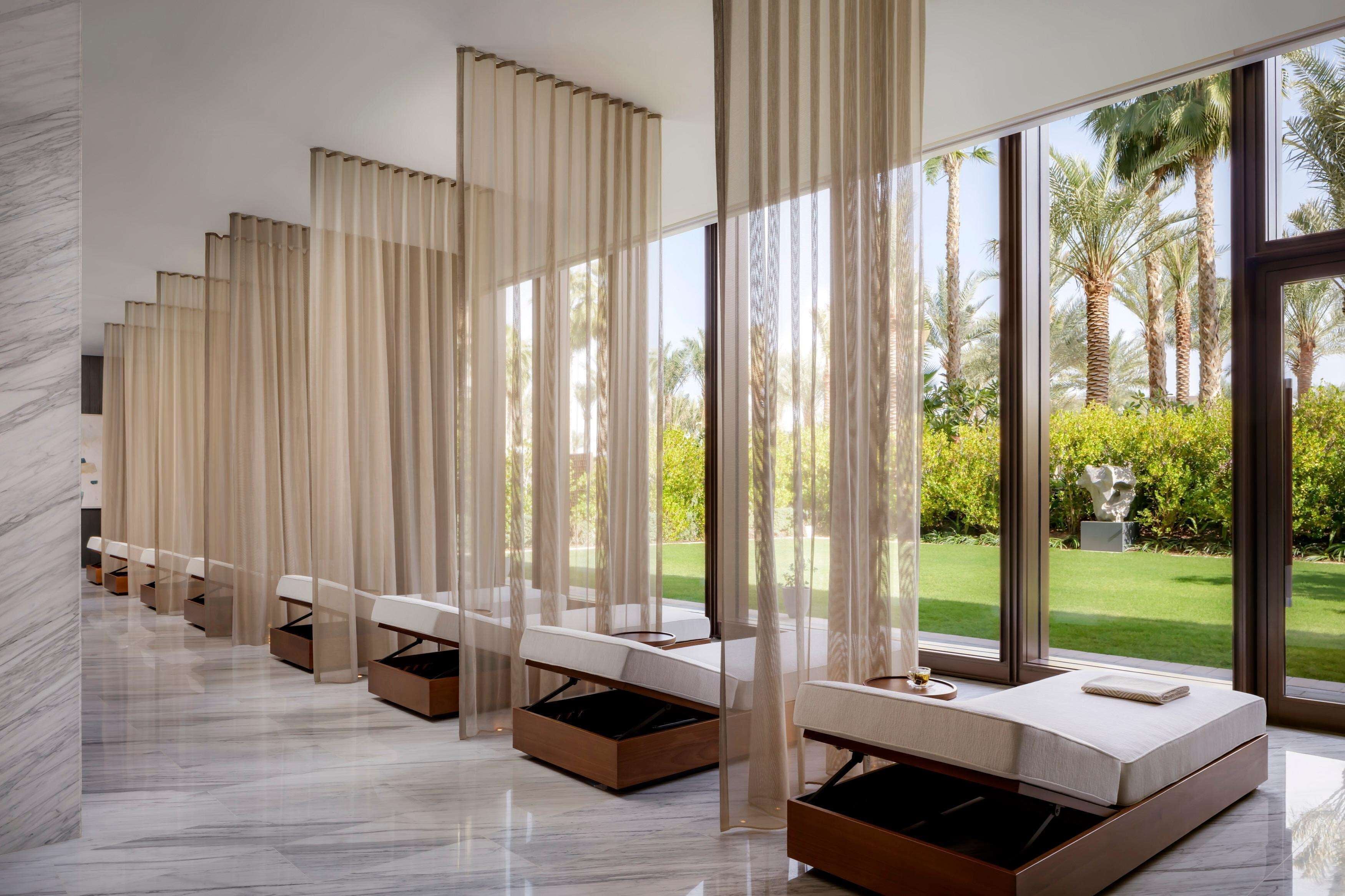 A modern hotel room with a large window, a bed with a wooden frame, and a series of chairs with storage drawers.