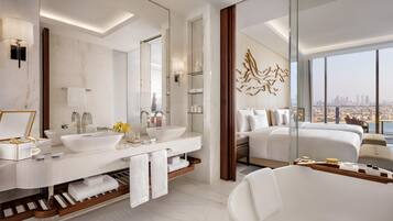A modern hotel bathroom with a large mirror, two sinks, a bathtub, and a city view.