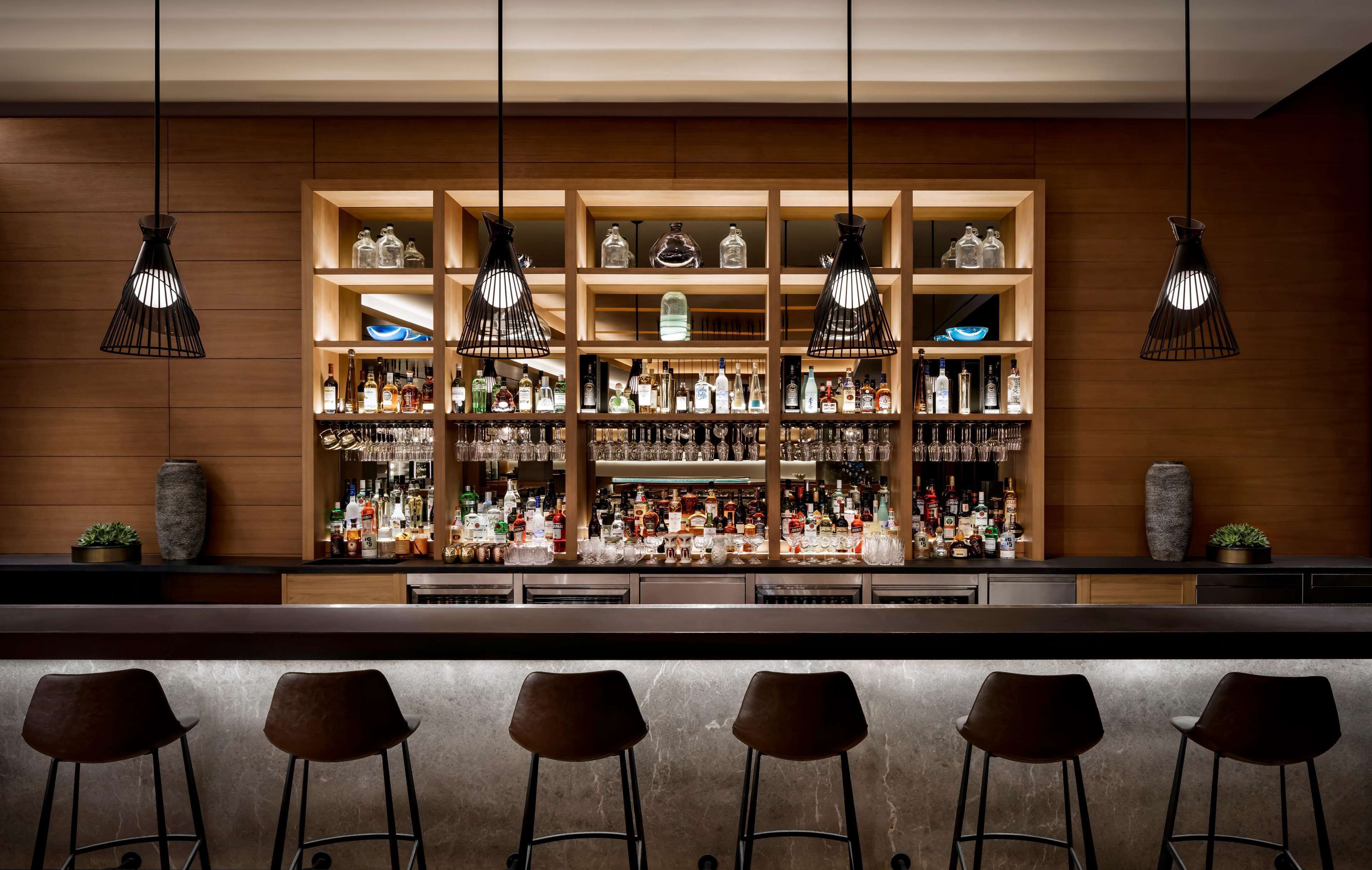 A bar area with multiple shelves of liquor bottles, hanging pendant lights, and bar stools.