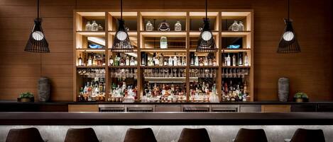A bar area with multiple shelves of liquor bottles, hanging pendant lights, and bar stools.