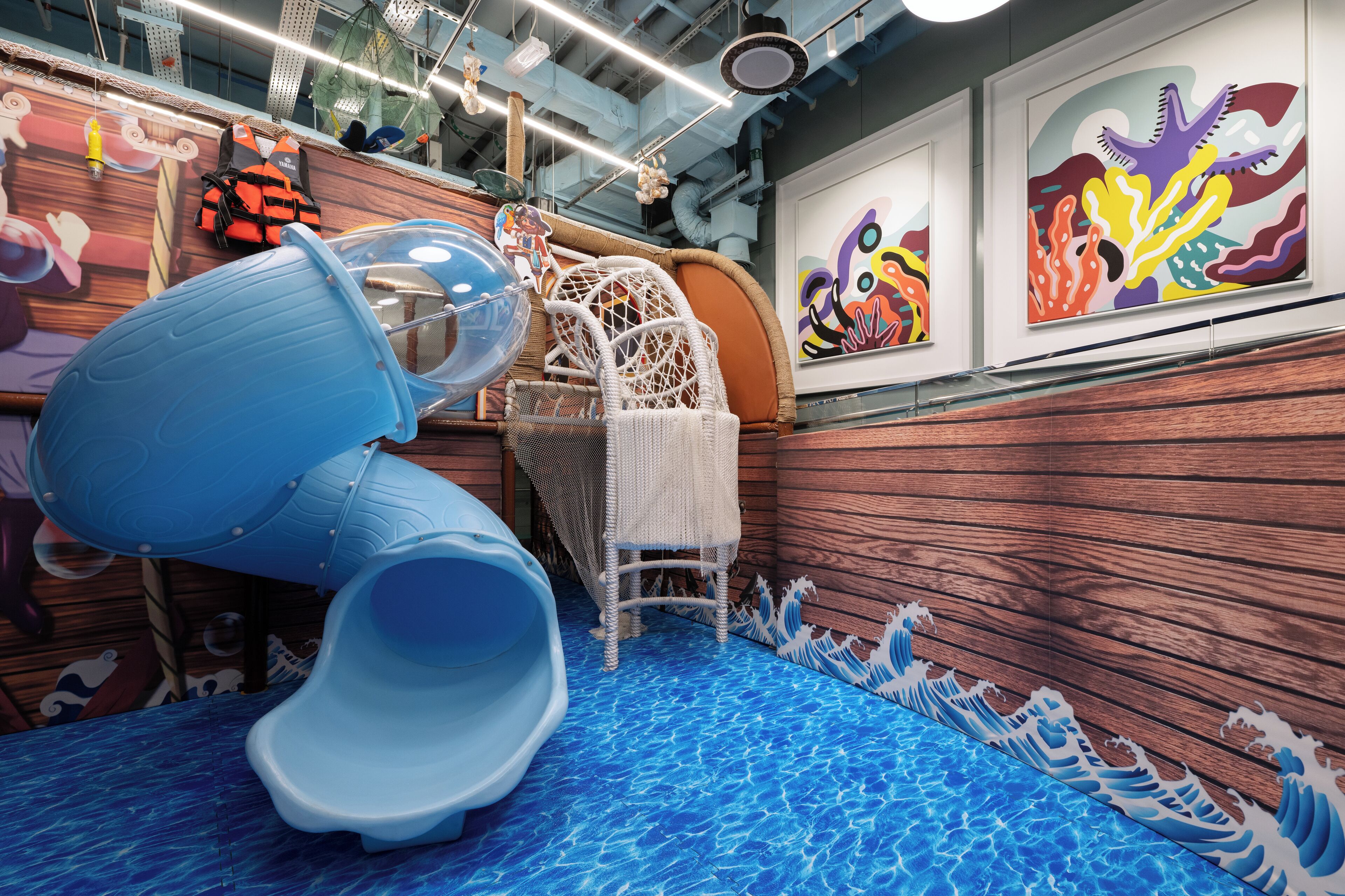 A children's play area with a slide, a playhouse, and artwork on the walls.