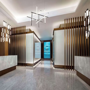 A modern reception area with a wooden reception desk, a logo on the wall, and a unique ceiling light fixture.