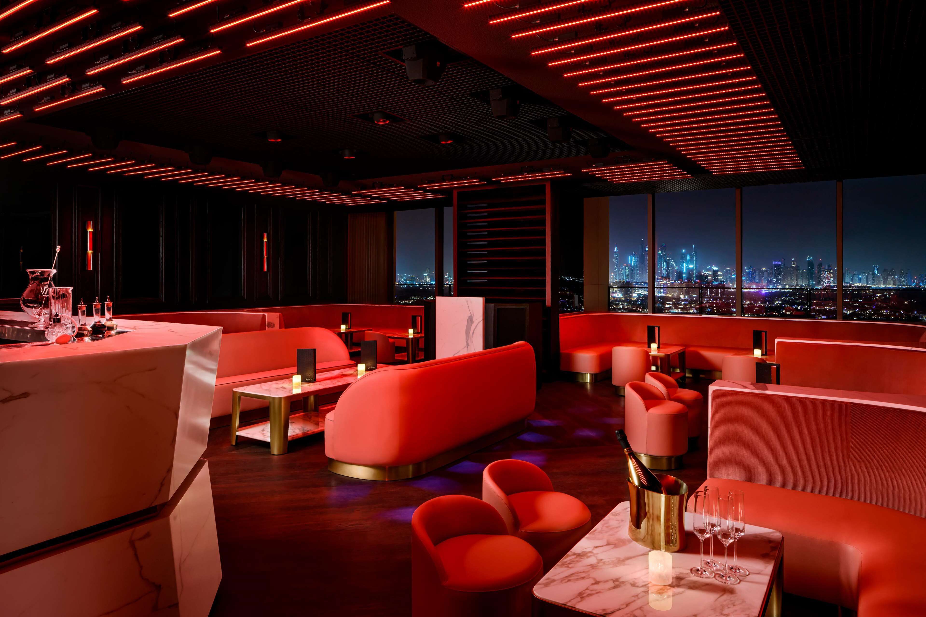 A modern lounge with red seating, a bar area, and a city view.