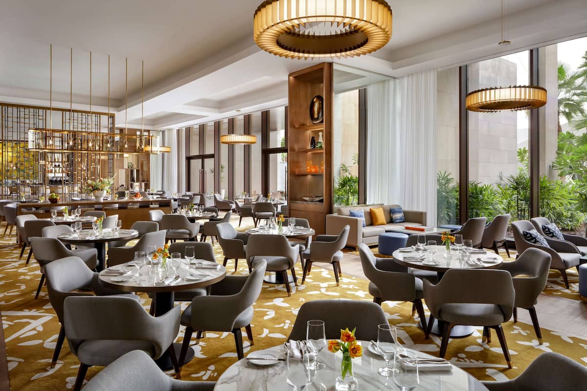 A spacious dining area with round tables, modern chairs, and pendant lighting.