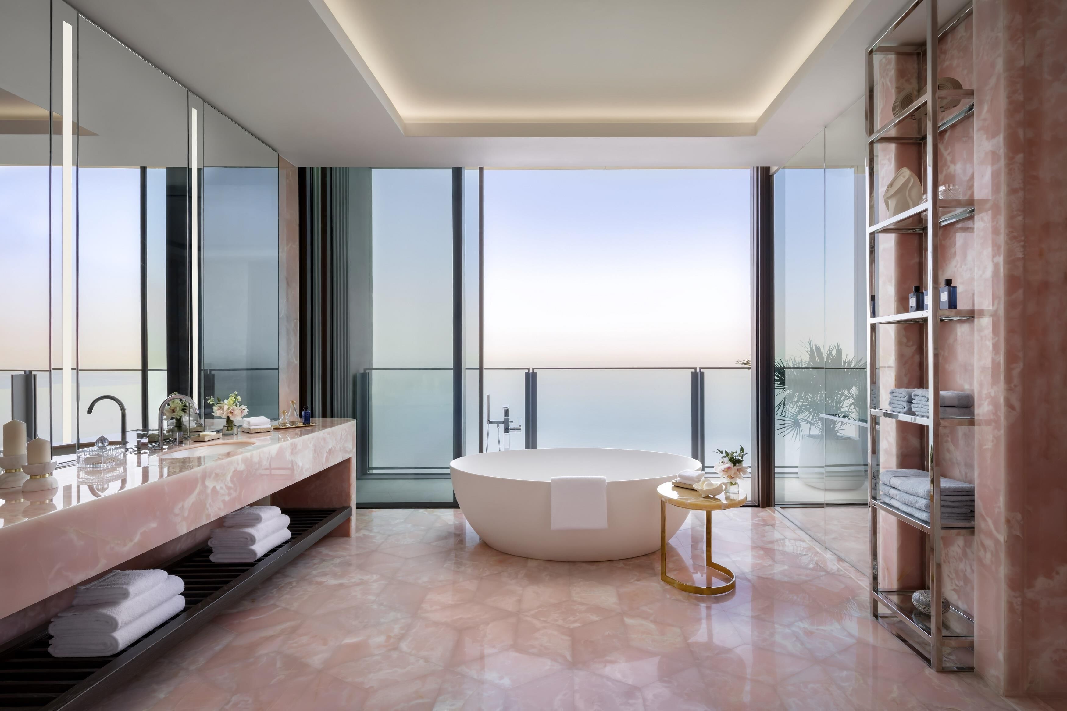 Une salle de bain moderne dotée d’une grande baignoire, d’un meuble-lavabo avec miroir et d’une grande fenêtre offrant une vue sur la ville.