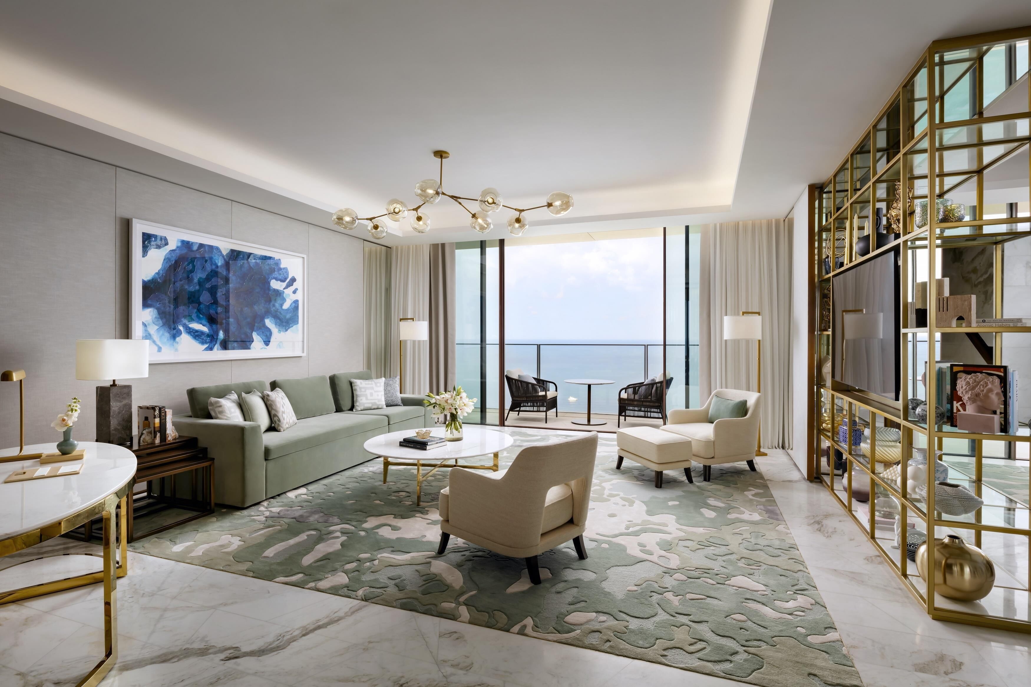 Een moderne hotelkamer met een groot raam, een groene bank, een witte salontafel en een boekenkast met gouden lijst.