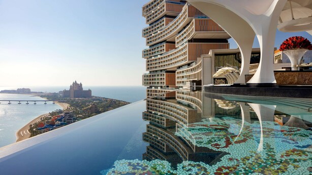 A modern hotel with a pool, a view of the beach, and a bridge in the background.