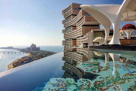 A modern hotel with a pool, a view of the beach, and a bridge in the background.
