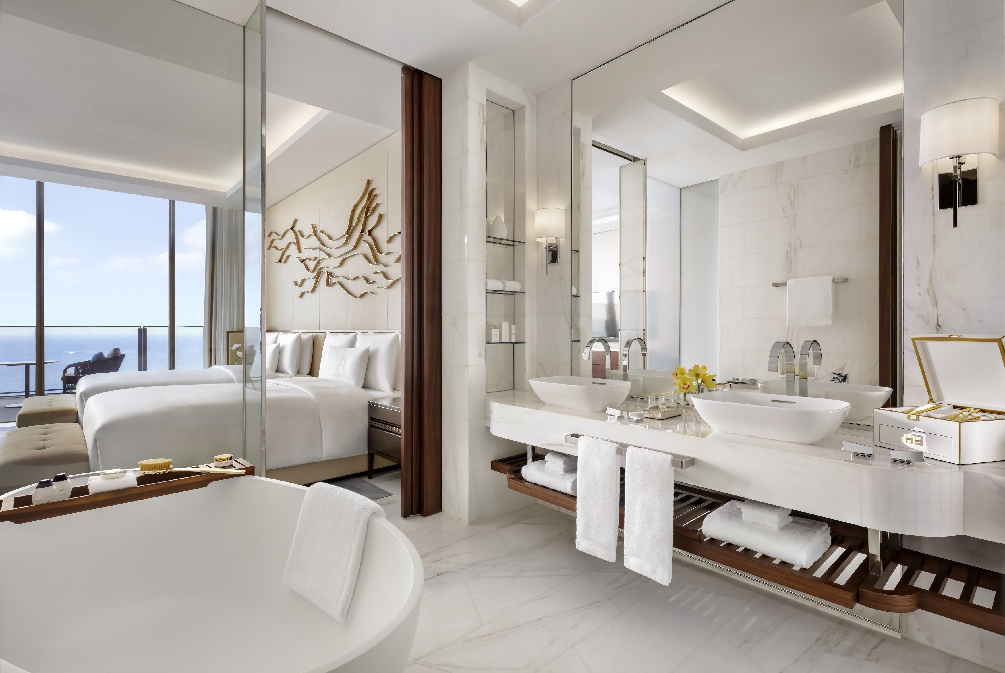A modern hotel bathroom with a large mirror, a bathtub, a vanity with a large sink, and a shower area.