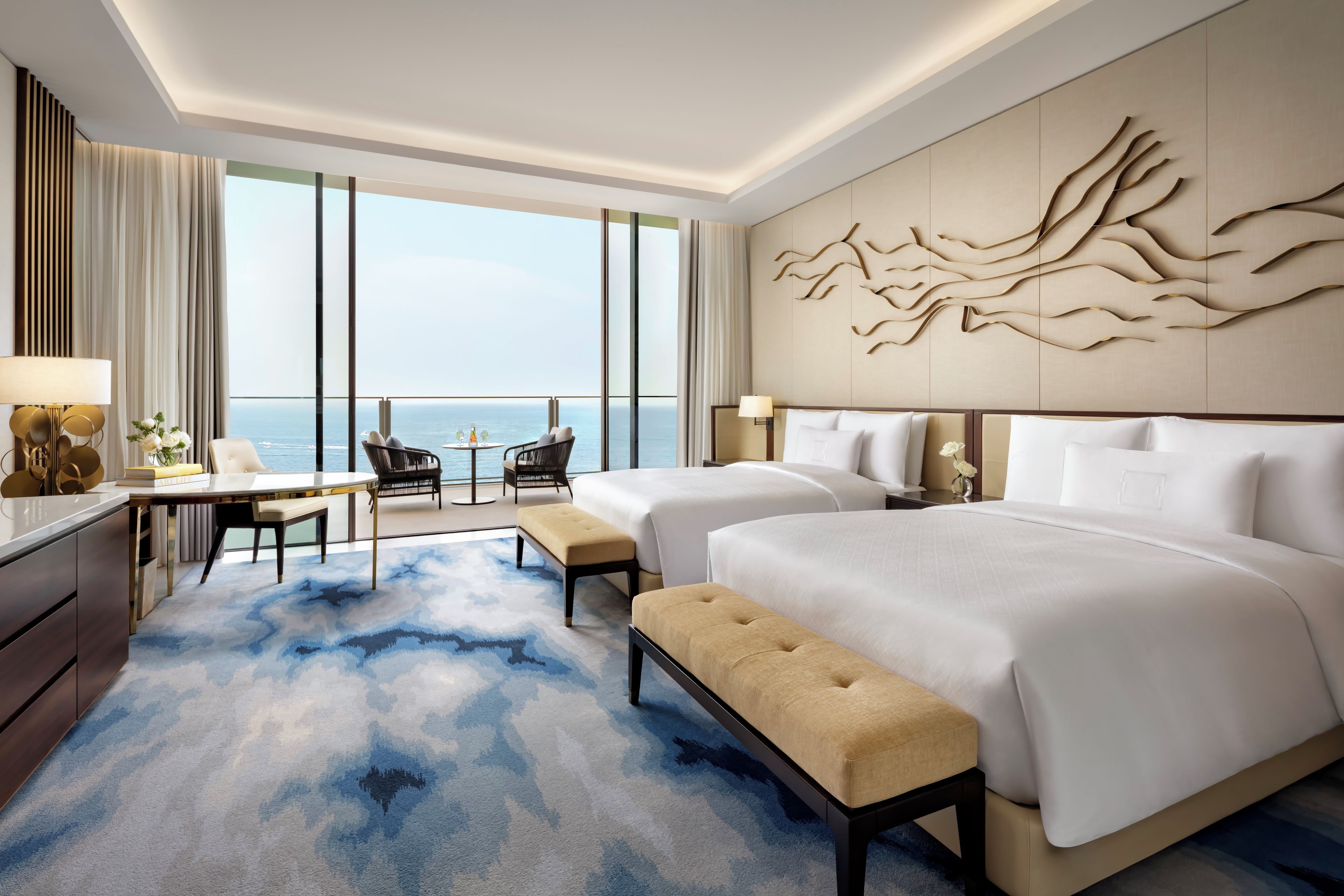 A hotel room with a large bed, a smaller bed, a desk, and a seating area with a view of the sea.