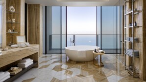 A modern bathroom with a freestanding bathtub, a vanity with shelves, and a large window offering a view of the ocean.