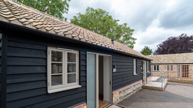 A small building with a tiled roof, a door, and a small set of stairs leading to a porch. - MJP @ The Shepherds (Cambridge)