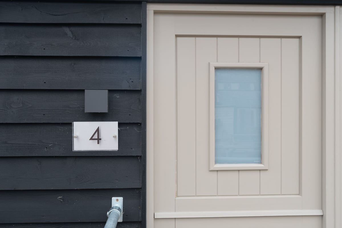 A house number '4' on a dark wooden wall, a white door with a window, and a visible electrical outlet.