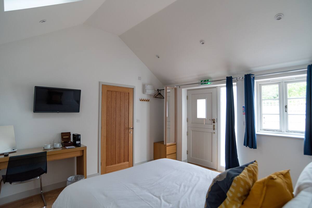 A hotel room with a bed, a desk with a chair, a television, and a window with curtains.