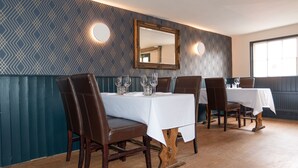 A dining area with a patterned wall, a mirror, and wooden chairs and tables. - MJP @ The Shepherds (Cambridge)