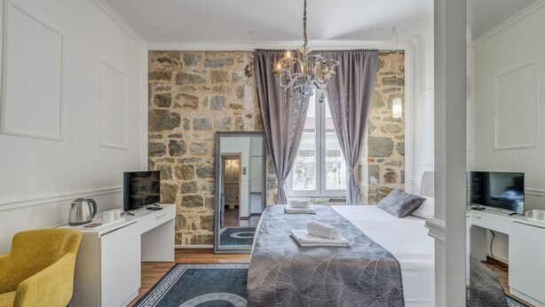 A hotel room with a stone wall, a bed with a patterned bedspread, a desk with a computer, a chair, and a TV.