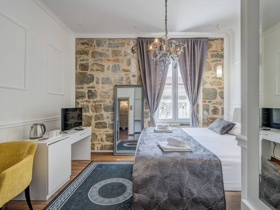 A hotel room with a stone wall, a bed with a patterned bedspread, a desk with a computer, a chair, and a TV.