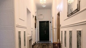 A hallway with wooden flooring, white walls, and a chandelier.