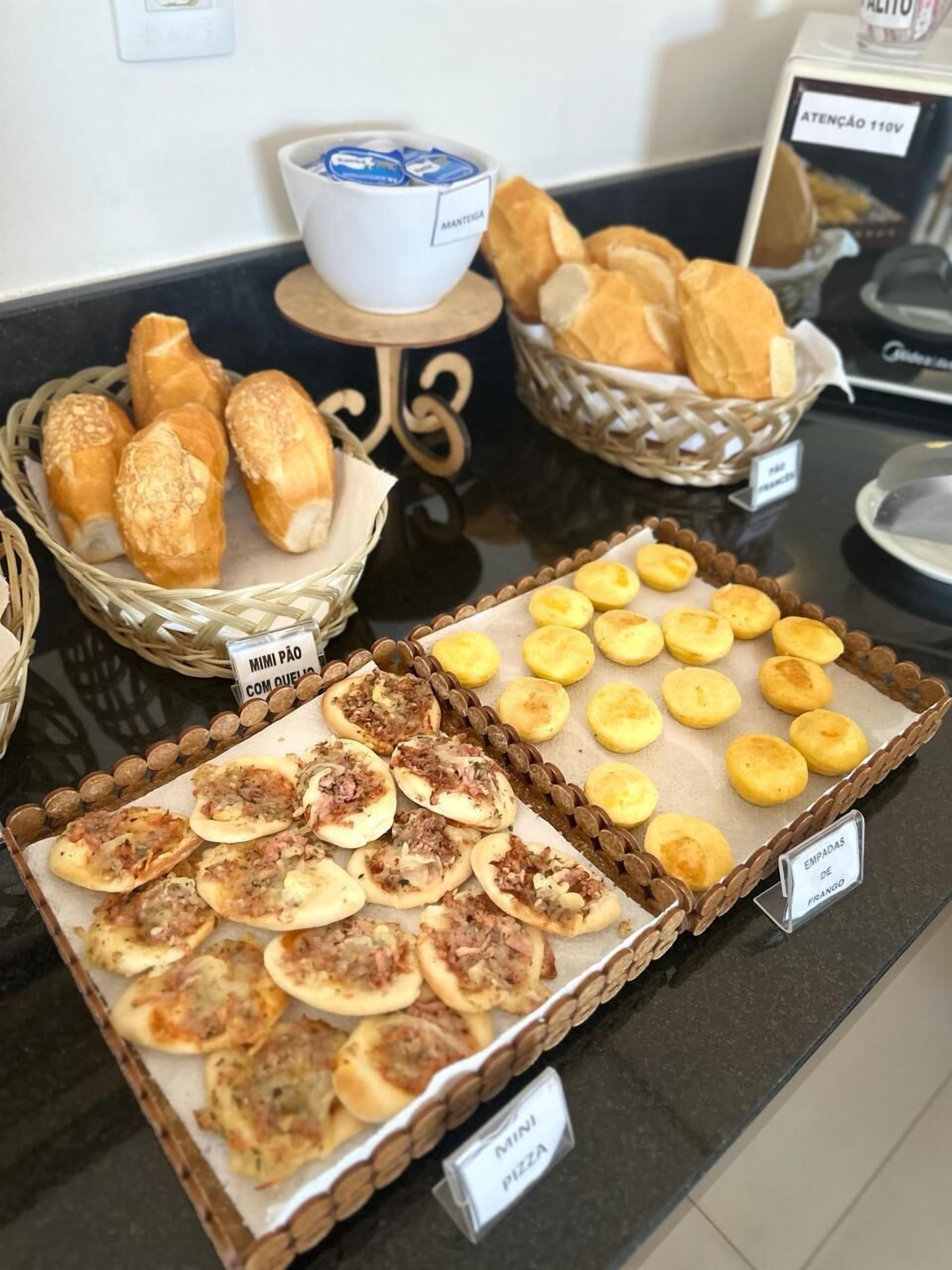 Buffet com diversos itens, incluindo mini pizzas, mini pão de queijo e mais mini pão de queijo.