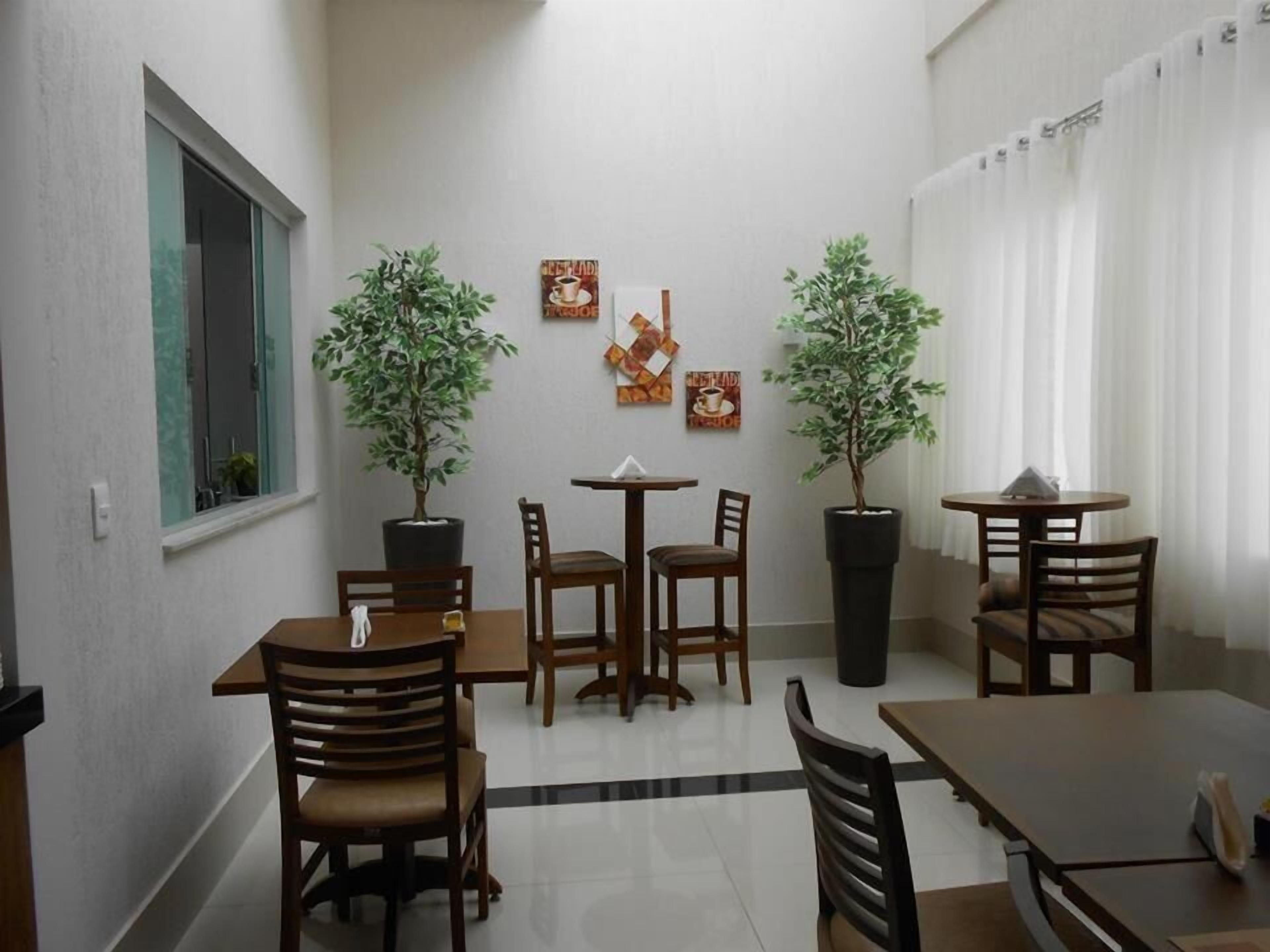 Un comedor con mesas y sillas de madera, plantas en macetas y obras de arte en las paredes.