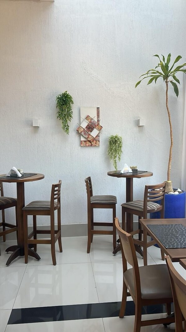 Un espace repas avec des tables et des chaises en bois, une plante en pot et une œuvre d’art accrochée au mur.