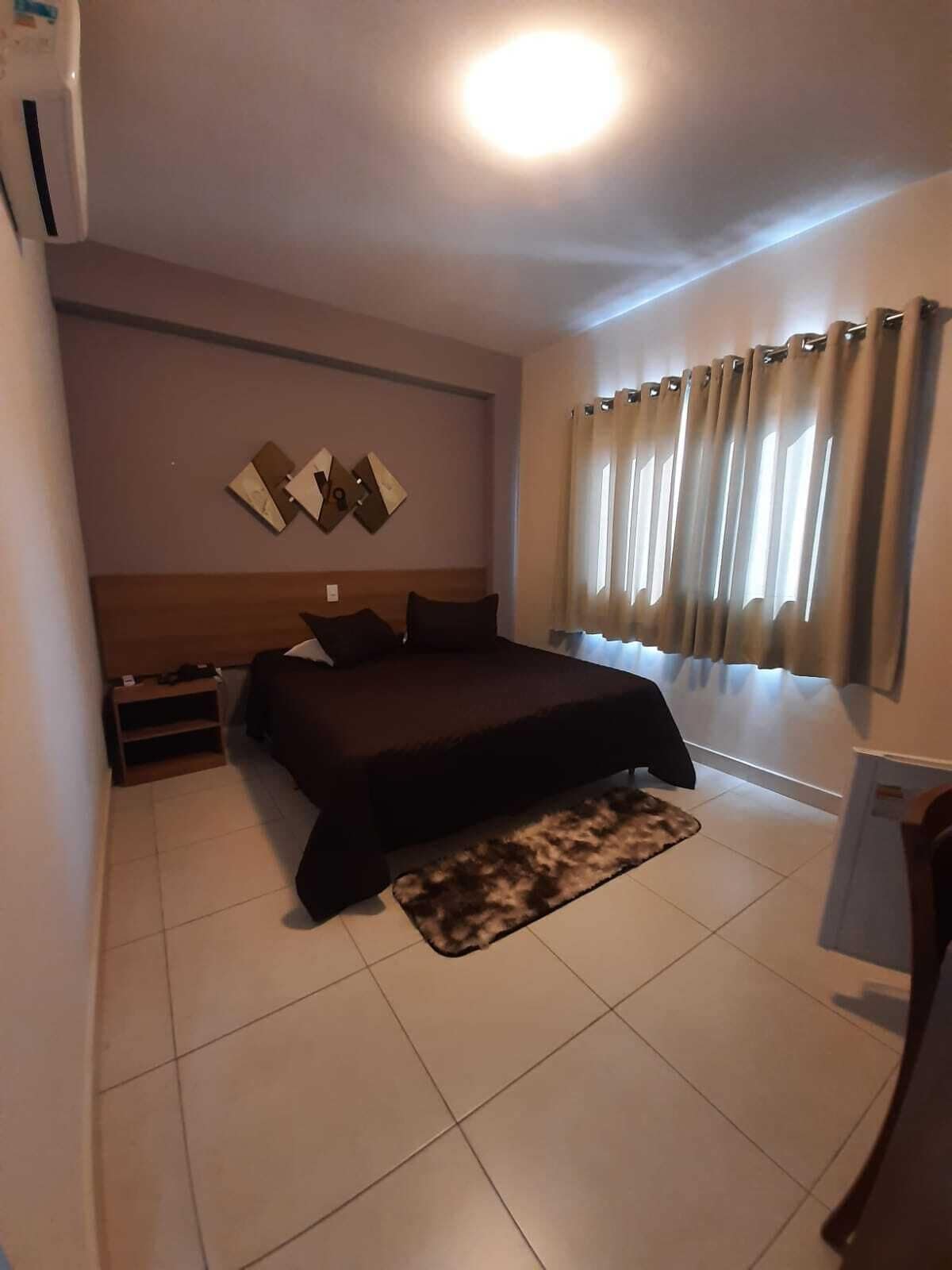 Une chambre à coucher avec un lit, une table de chevet, une lampe, un tapis et une fenêtre avec des rideaux.
