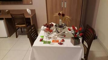 Una mesa de comedor decorada con una botella de vino, copas, un frutero y un centro de mesa con rosas rojas.