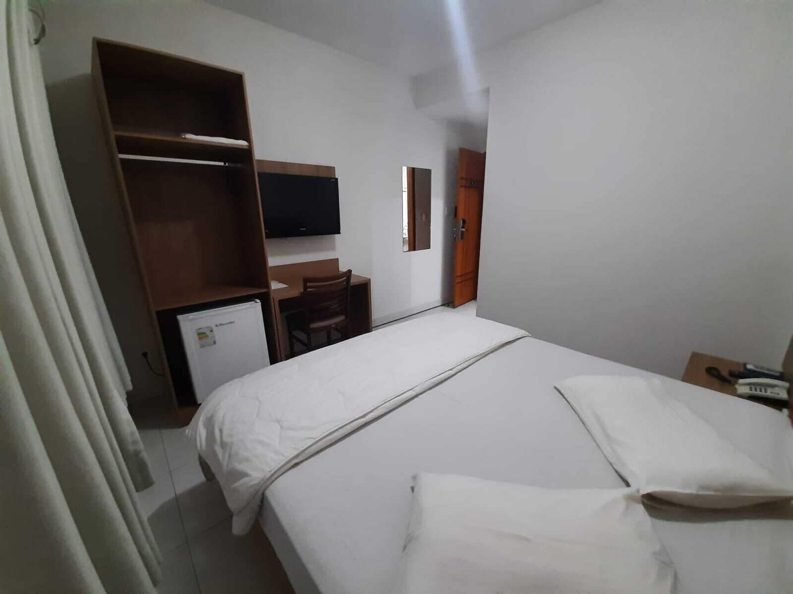 A hotel room with a bed, a desk, a television, and a wardrobe.