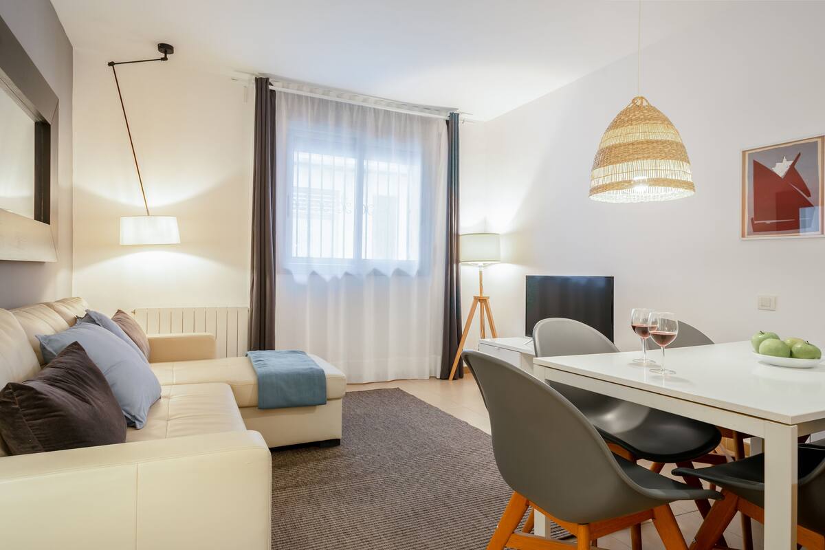 Uma sala de estar moderna com um sofá, uma mesa de jantar com cadeiras, um abajur e uma moldura com um quadro na parede.