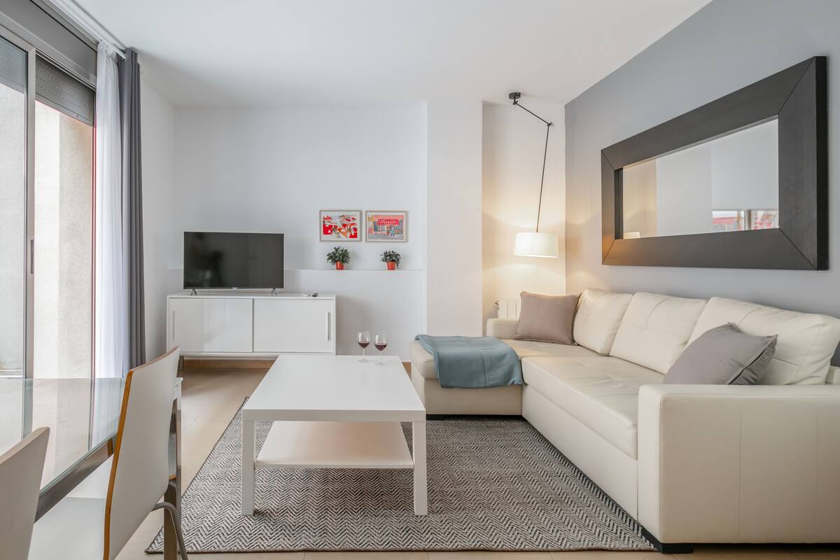 Uma sala de estar moderna com um sofá branco, uma mesa de centro, uma TV em um armário e duas fotos emolduradas na parede.