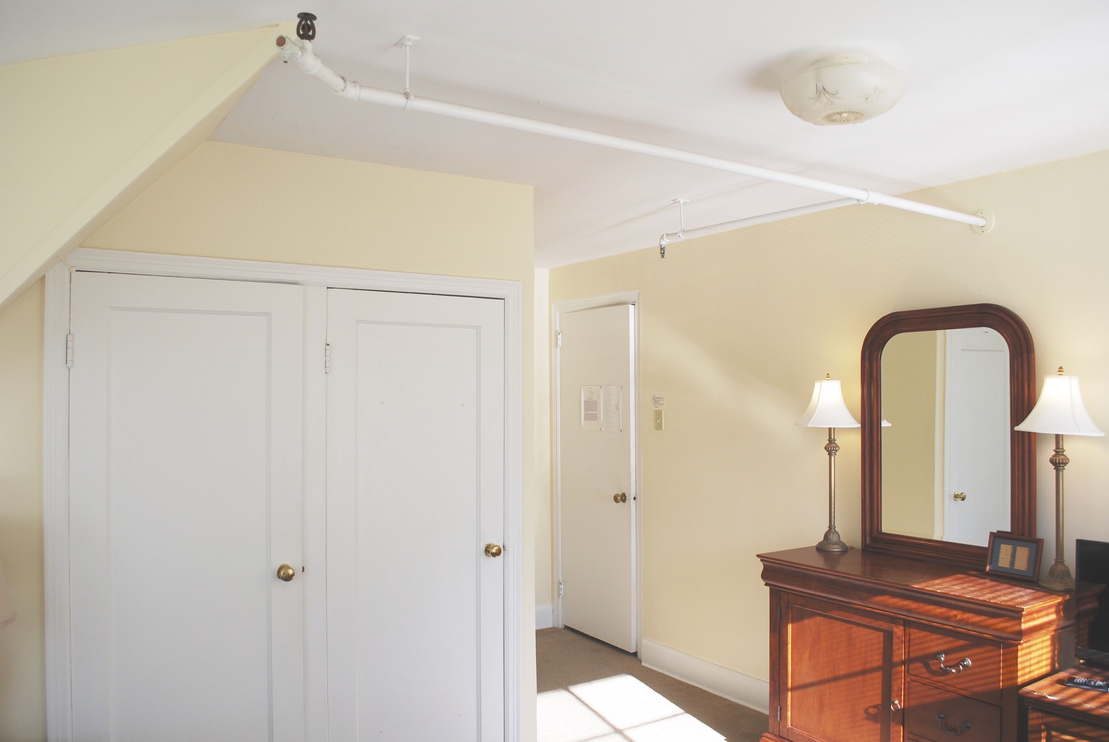 A room with two white doors, a wooden dresser with a mirror, and a ceiling light fixture.