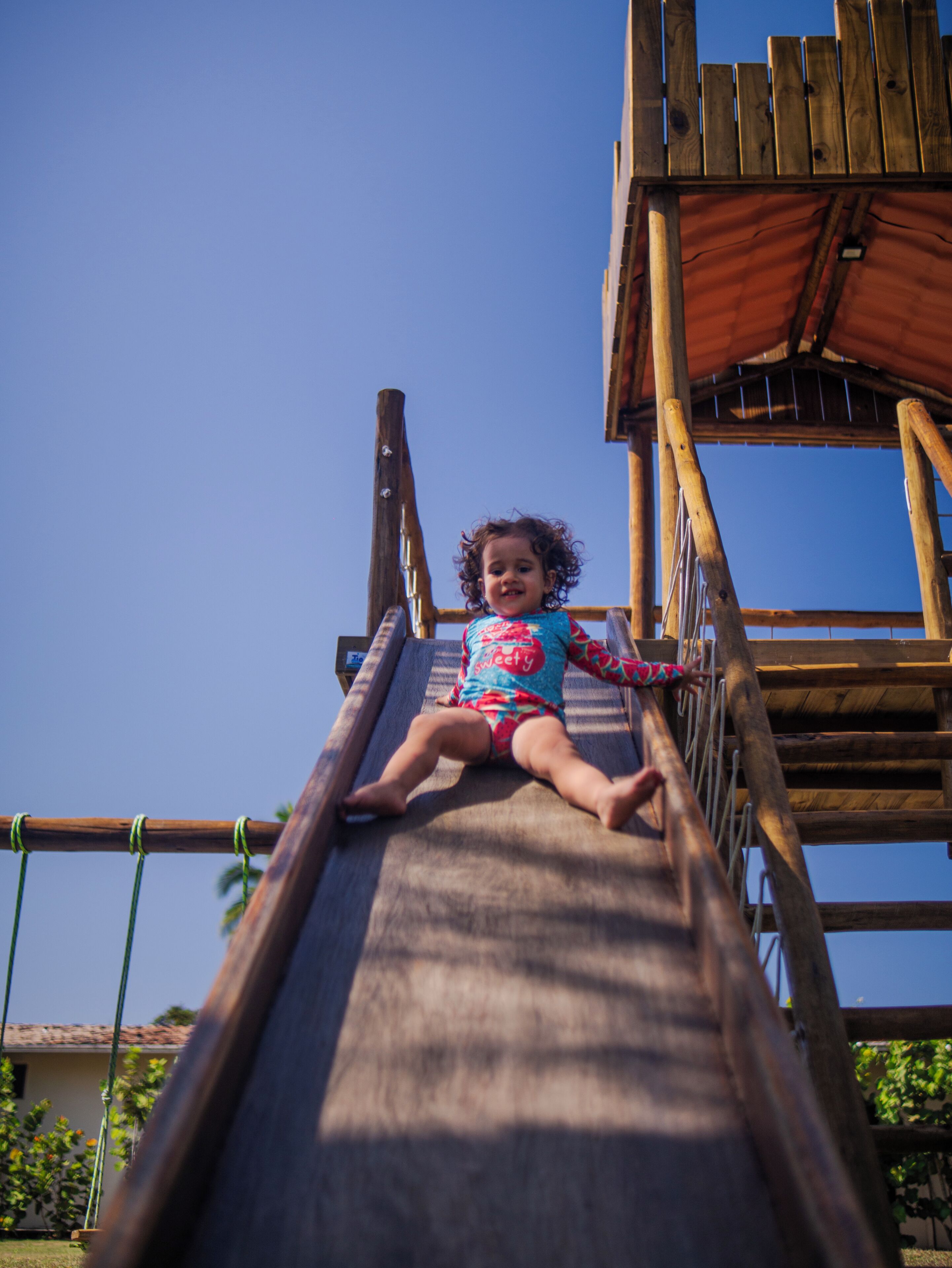 A child on a wooden slide with a clear blue sky in the background.