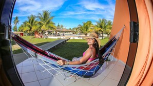 Una persona descansando en una hamaca en un balcón, con vista a una piscina y palmeras.