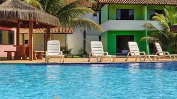 Relax by the serene pool surrounded by lounge chairs and a thatched-roof structure.