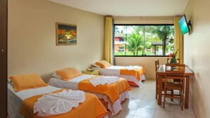Habitación de hotel con dos camas, un escritorio y una silla. Se ve una ventana con vistas a palmeras y un edificio.