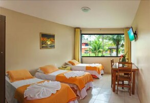 Habitación de hotel con dos camas, un escritorio y una silla. Se ve una ventana con vistas a palmeras y un edificio.