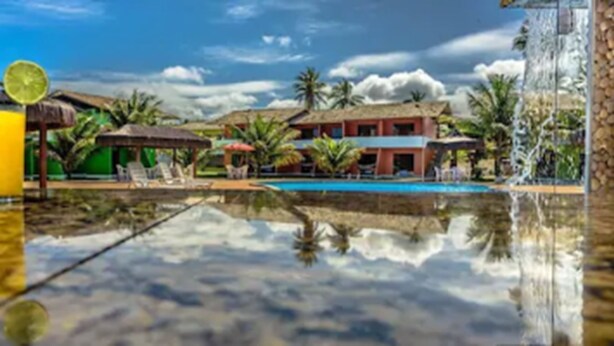 Vista de la piscina con cielo despejado, palmeras y un edificio de fachada roja.