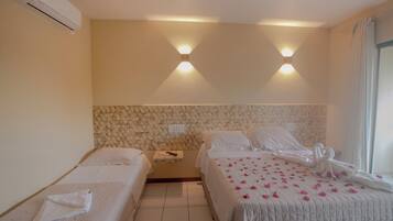 Quarto de hotel com duas camas de solteiro, piso de azulejos, ar condicionado na parede e uma janela com cortinas.
