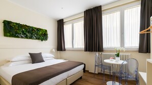 A neatly arranged hotel room with a bed, a small table with chairs, a radiator, and a window with curtains. - Demetra Guest House (Rome)
