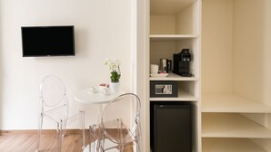 A modern room with a flat-screen TV, a small table with a potted plant, two clear chairs, and a compact refrigerator. - Demetra Guest House (Rome)