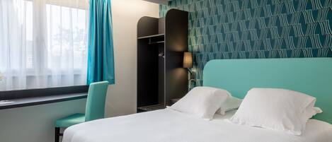 A hotel room with a bed, a chair, a wardrobe, and a window with curtains.