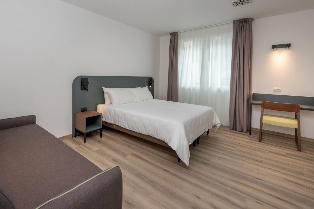 Una habitación de hotel moderna con cama, sofá, escritorio y silla.