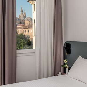 A hotel room with a large window, a bed, a nightstand, a vase with flowers, and a wall-mounted light fixture. - Hotel Canton dell Orto (Padova)