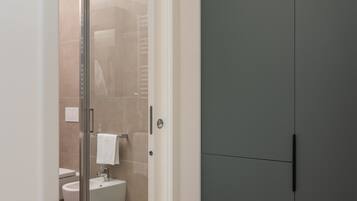 A modern bathroom with a glass shower door, a white sink, and a toilet visible through the door.