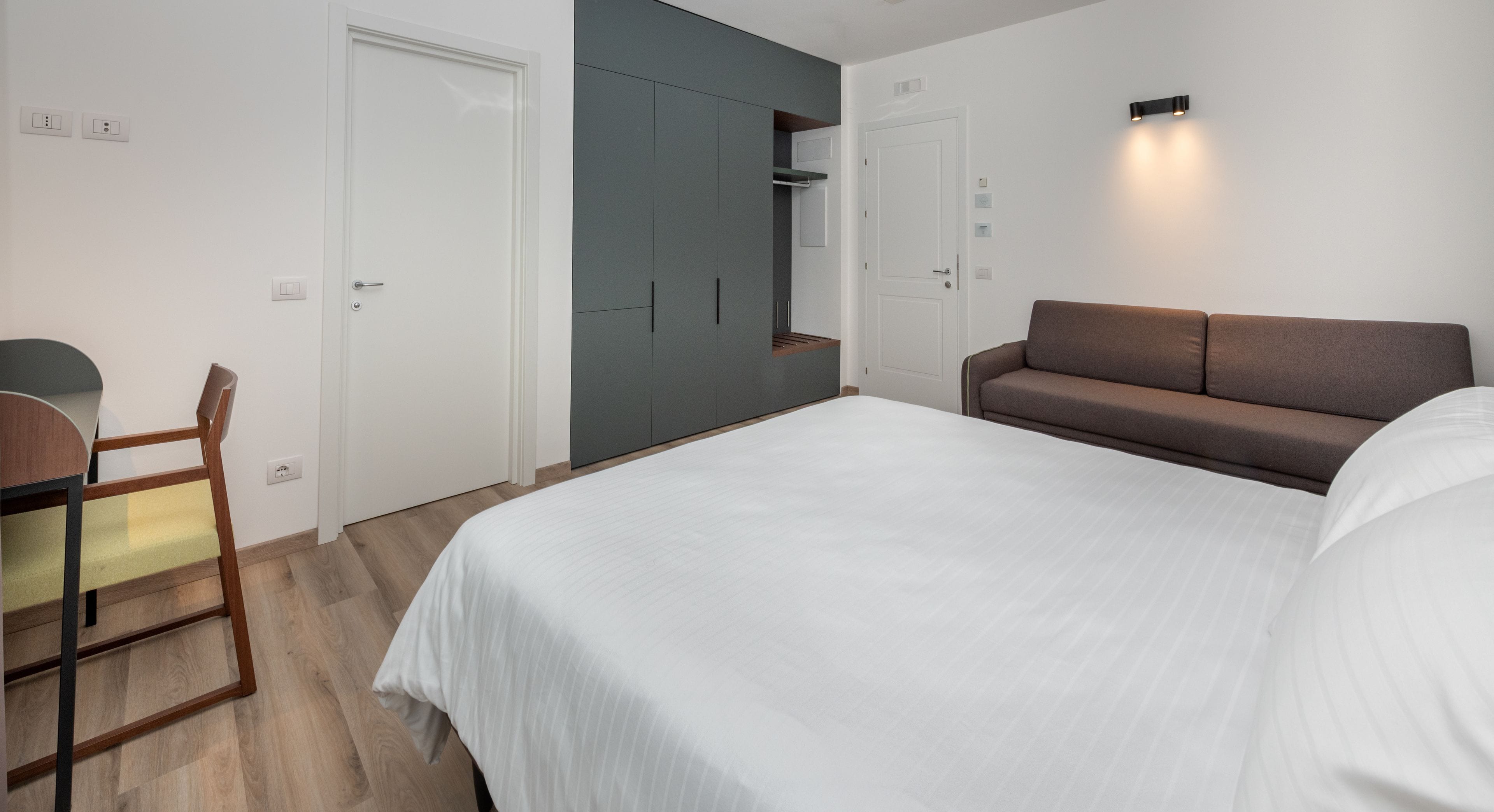 A bedroom with a bed, a desk, a chair, a sofa, and a wardrobe.