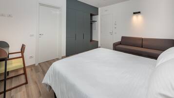 A bedroom with a bed, a desk, a chair, a sofa, and a wardrobe.