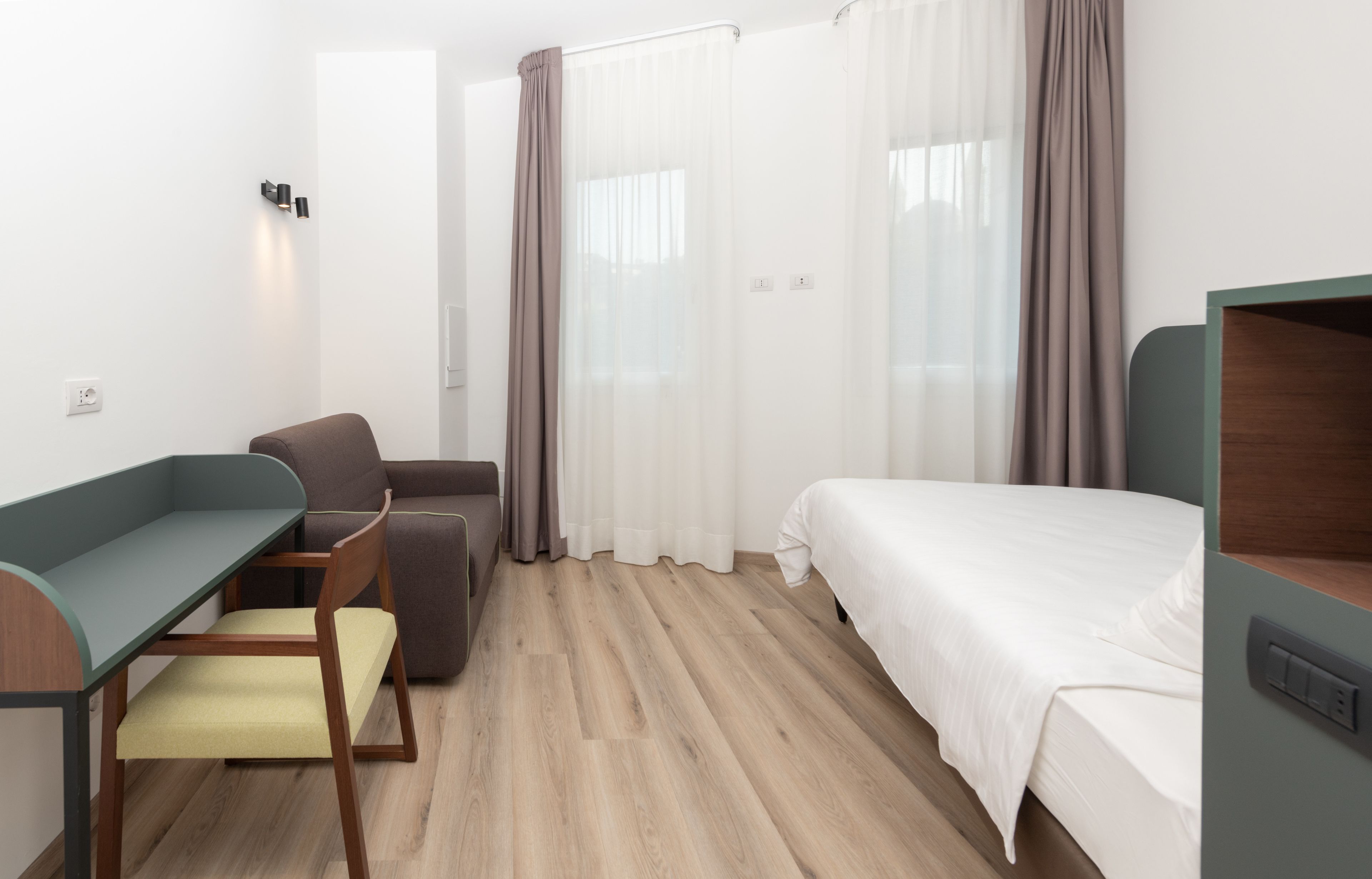 Ett hotellrum med en säng, ett skrivbord med en stol, en soffa och gardiner.
