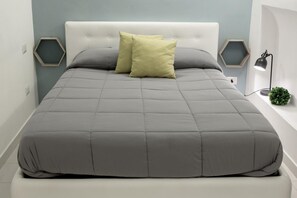 A neatly made bed with a grey quilt and two pillows, a white headboard, and hexagonal wall decorations. - B&B Le Caravelle (Monopoli)