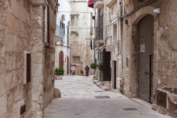 A narrow street with stone buildings, a person walking, and a sign for a bed and breakfast. - B&B Le Caravelle (Monopoli)